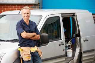 Mature tradie wearing tool belt leaning against white van 