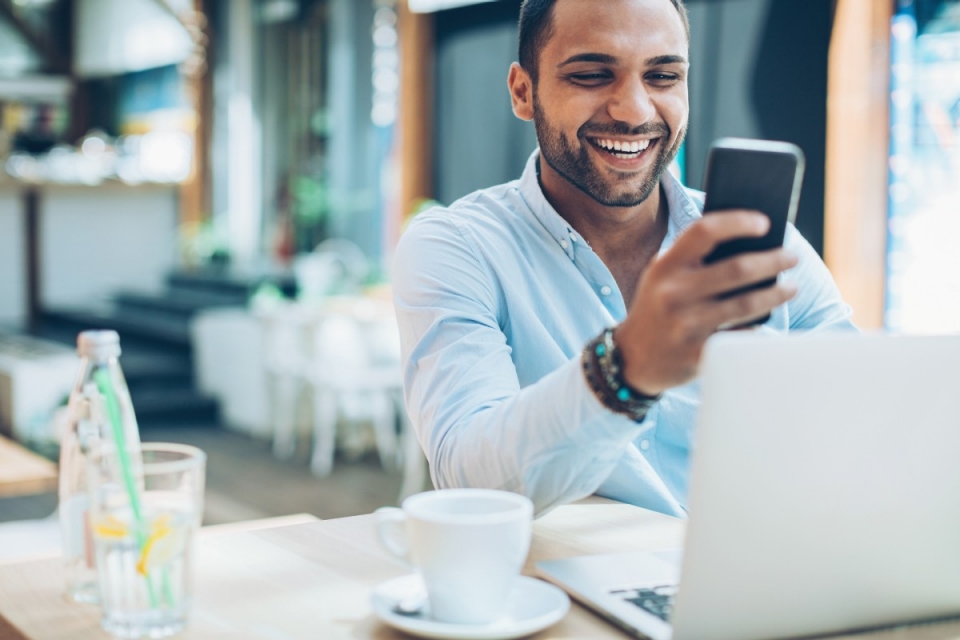 Smiling business man checking his phone in front of a laptop