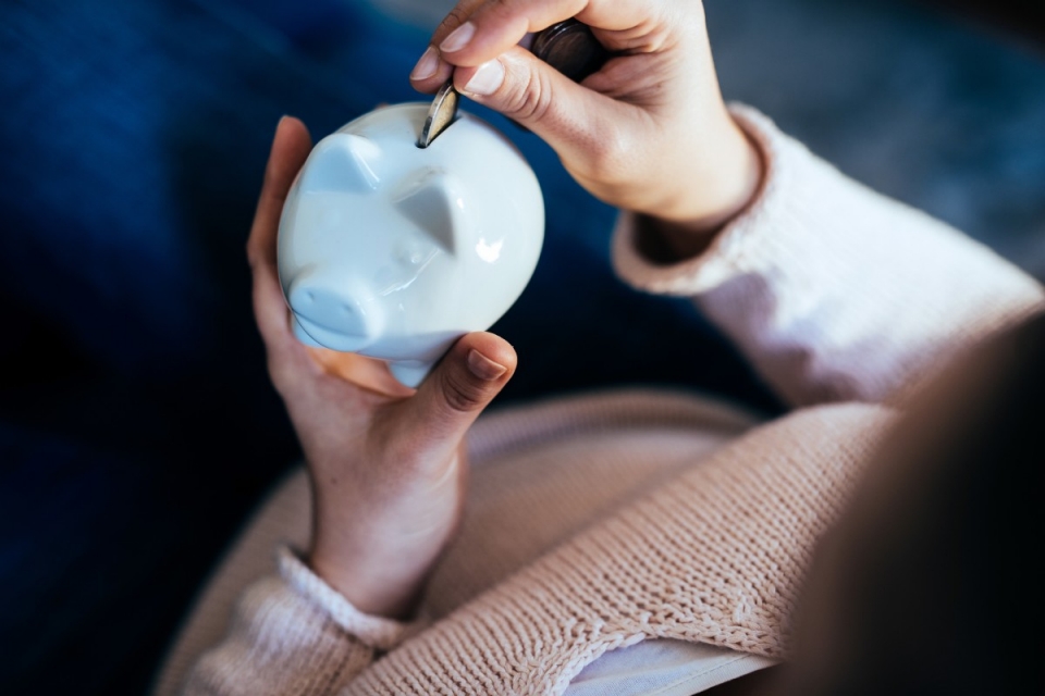 Close up of a female holding a piggy bank and putting a coin in it