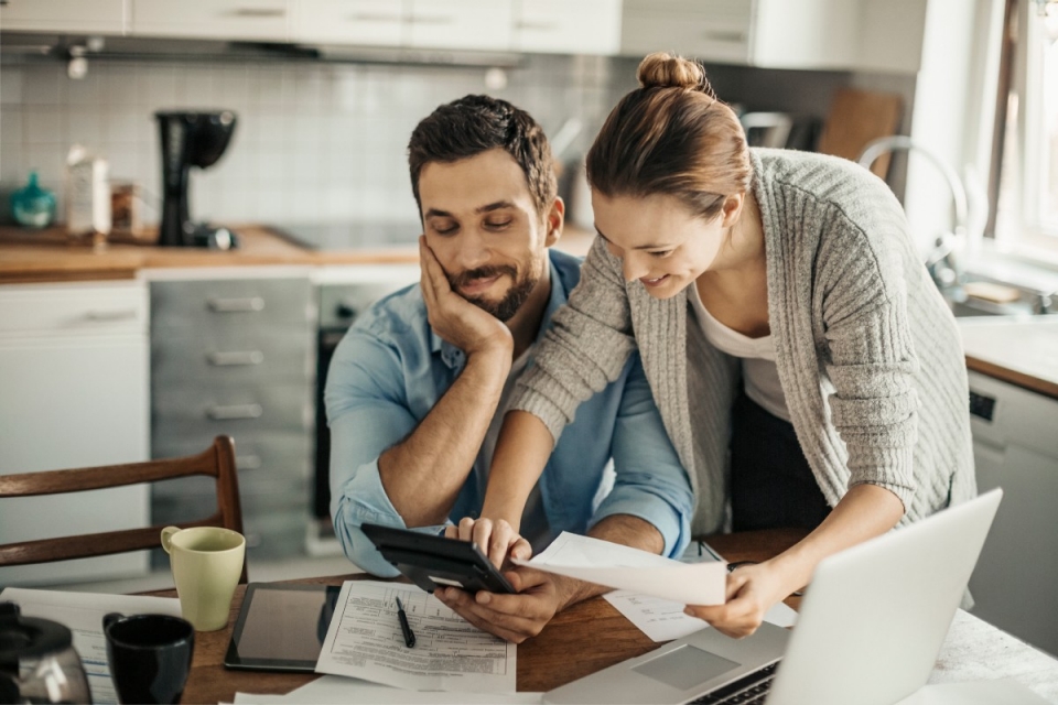 Young couple in bright kitchen doing paperwork and using a calculator