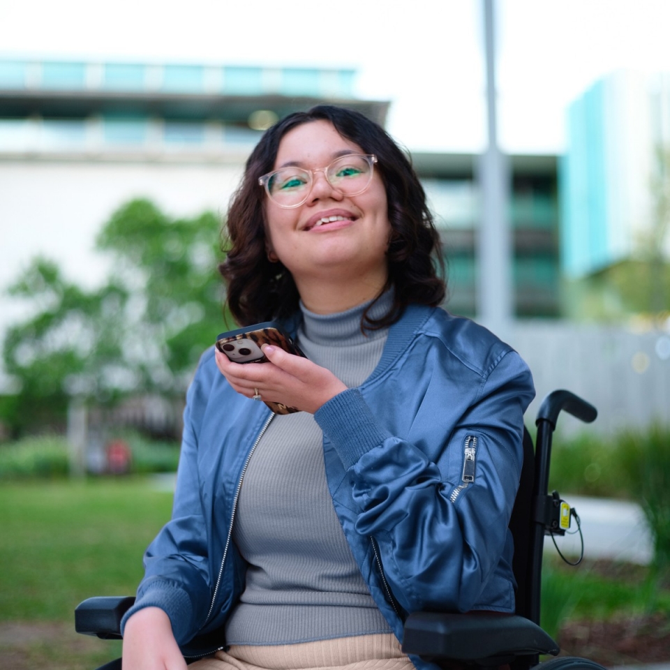 A woman in a wheelchair smiling and holding her phone
