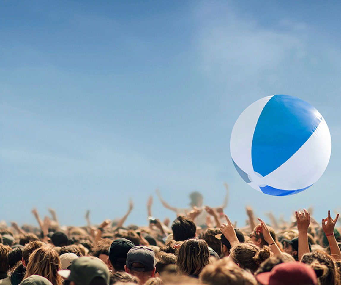 A crowd is tossing a blue and white striped ball into the sky.